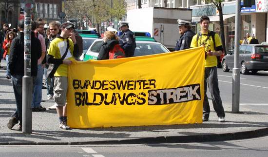Two people with yellow T-shirts hold a banner with the Bildungsstreik logo.